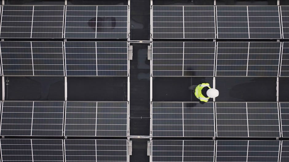 Aerial view of a worker inspecting solar panels on a rooftop, promoting renewable energy.